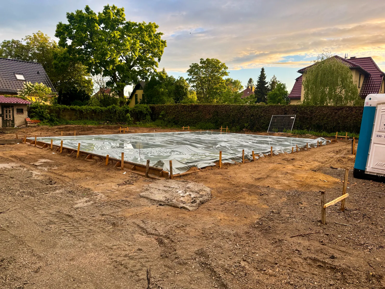 Weitläufige Baustelle mit einer frisch betonierten, vollflächig mit Folie geschützten Bodenplatte vor aufziehendem Abendwetter — vorbeugender Schutz des frischen Betons gegen Regen
