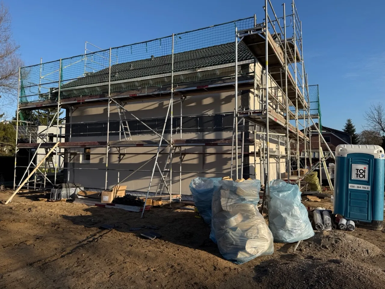 Eingerüstetes Fertigteilhaus in Berlin-Biesdorf während der Fassadenmontage mit fast fertiggestellter heller Putzfassade