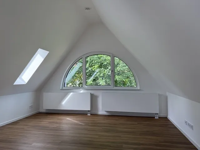 Helles Dachgeschoss-Studio eines Stadthauses im Wohnensemble CÖ Köpenick mit großem Rundbogenfenster in der Giebelseite und Dachflächenfenstern