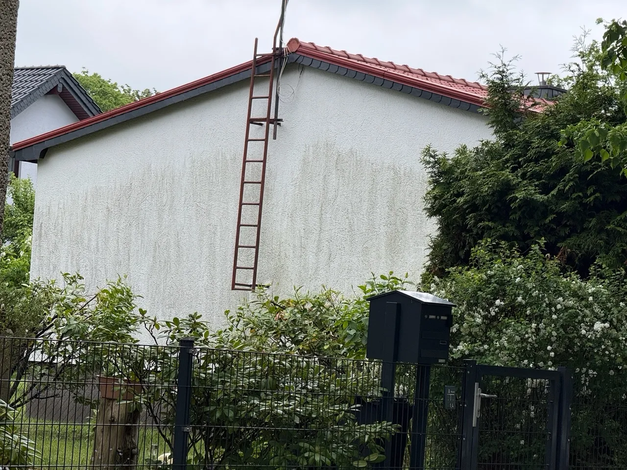 Helle WDVS-Putzfassade mit deutlichen senkrechten dunklen Ablaufspuren unterhalb der Dachrinne — Wasser nimmt Schmutz und Schwebstoffe auf und transportiert sie über die Putzoberfläche