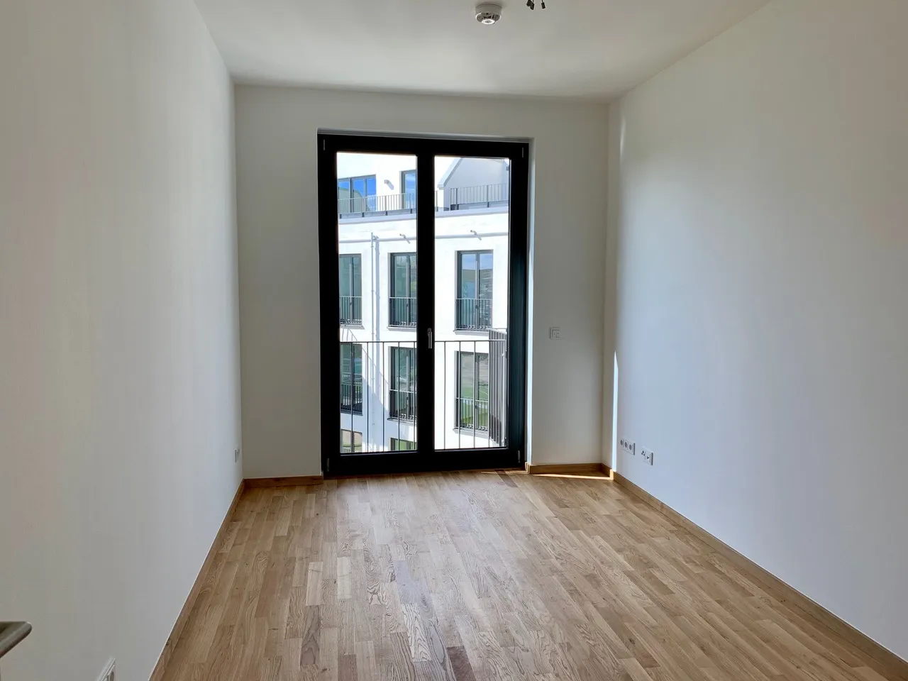 Zimmer mit französischem Balkon und Blick auf gegenüberliegende Neubauten