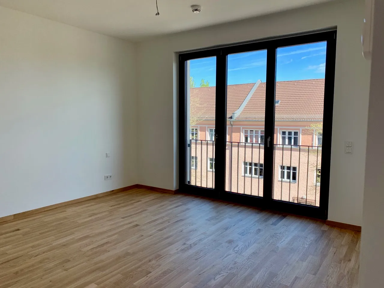 Wohnraum mit Mehrschichtparkett und bodentiefen Fenstern mit Balkonzugang